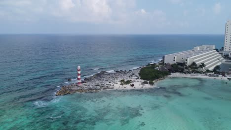 Aerial-Drone-view-zooming-out-of-Punta-Cancun-Lighthouse,-a-landmark-in-Cancun,-Mexico,-surrounded-by-turquoise-water-of-the-Caribbean-sea