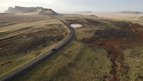 Aerial-following-black-car-drive-through-vast-Iceland-volcanic-mountain-panorama