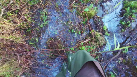 Man-in-tall-rubber-boots-walking-in-swampy-landscape,-POV-slow-motion-view