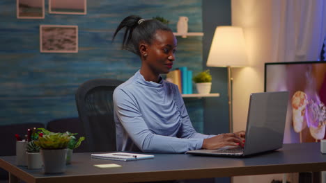 Black-woman-typing-on-computer-smiling-late-at-night