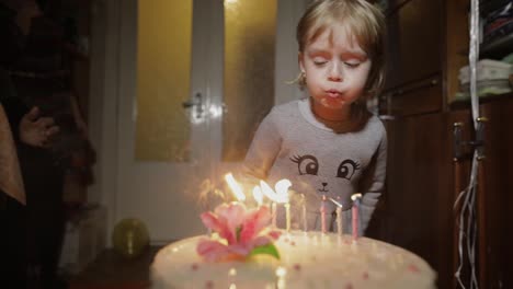 Little-cute-girl-blows-out-candles-on-birthday-cake-at-home-party