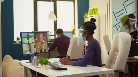 African-worker-with-face-mask-talking-on-videocall-in-office-room
