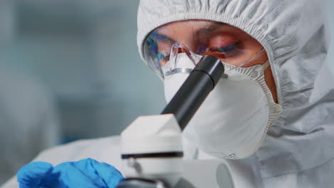 Lab-technician-with-protection-suit-examining-samples-using-microscope