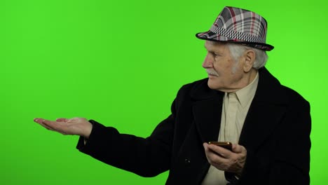 Älterer-Großvater-Benutzt-Smartphone-Und-Zeigt-Mit-Der-Hand-Auf-Etwas