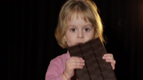 Attractive-child-eating-a-huge-block-of-chocolate.-Cute-blonde-girl