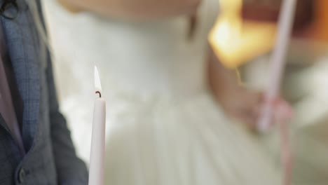 The-bride-and-the-groom-stand-in-church,-holding-candles-in-their-hands