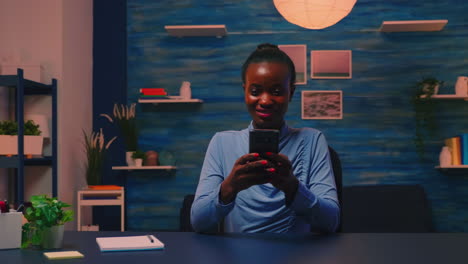Black-businesswoman-browsing-using-smartphone-sitting-in-living-room