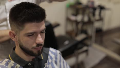 Client-with-black-beard-during-hair-cut-in-barber-shop.-Groom,-masculine