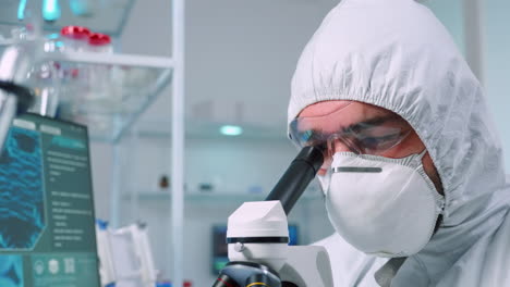 Biochemist-in-ppe-suit-looking-through-a-microscope-during-experiment