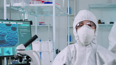 Microbiologist-sitting-in-laboratory-wearing-ppe-suit-looking-at-camera