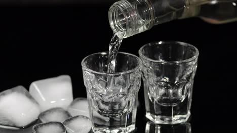 Pour-vodka-into-shot-glasses-with-ice-cubes-placed-on-a-black-background