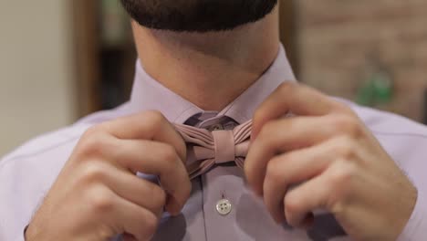 Groom-adjusts-bow-tie-in-barbershop-background.-Preparing-to-go-to-the-bride