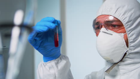 Scientist-in-coverall-examining-blood-test-tubes-at-laboratory