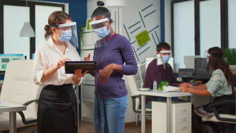 Worker-with-face-mask-discussing-with-black-woman-holding-tablet