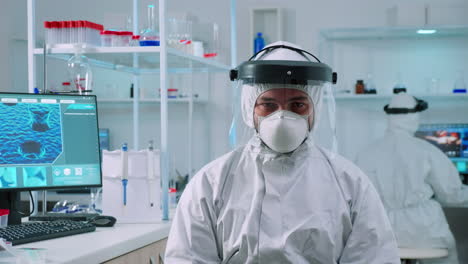 Doctor-man-looking-at-camera-sitting-in-lab-dressed-in-ppe-suit
