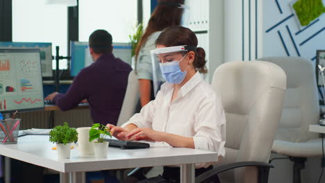 Manager-with-face-mask-typing-on-computer-and-looking-on-camera