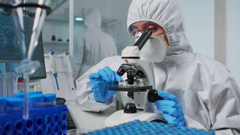 Scientist-wearing-ppe-suit-looking-at-samples-under-microscope
