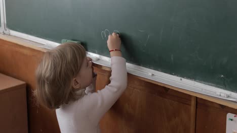 Girl-drawing-at-blackboard-using-a-chalk-in-classroom.-Education-process