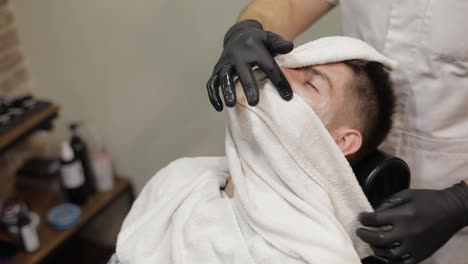 Client-with-black-beard-during-beard-shaving-in-barber-shop.-Groom,-masculine