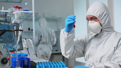 Scientist-in-sterile-chemistry-suit-analysing-blood-sample-from-test-tub