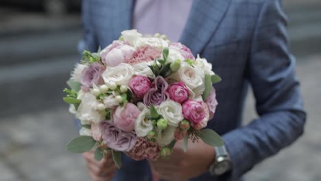 Groom-with-wedding-bouquet-in-his-hands-on-the-street.-Pink-shirt,-blue-jacket