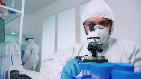 Scientist-in-ppe-suit-conducting-experiment-using-microscope