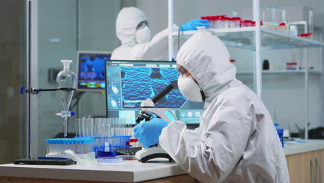 Chemist-researcher-in-coverall-looking-at-bacteria-sample-from-glass