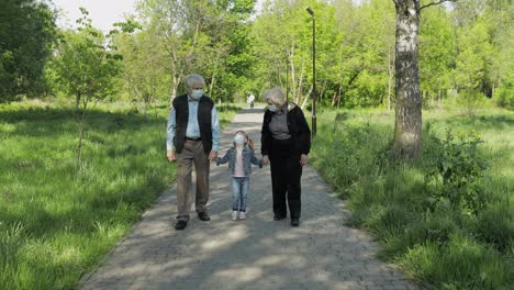 Old-grandparents-with-granddaughter-in-medical-masks-walk-in-park.-Coronavirus