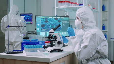Chemist-in-protection-suit-typing-on-pc-and-analyzing-virus-sample