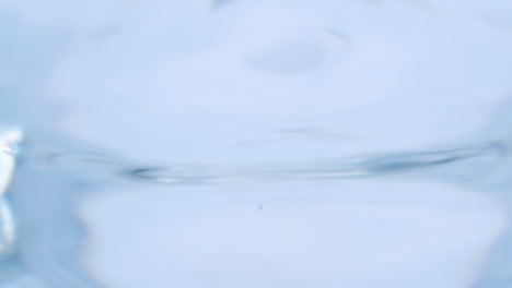 Flüssigkeitstropfen-Erzeugen-Wellen-Und-Winzige-Blasen-In-Einem-Glas,-Das-Mit-Frischem,-Klarem-Und-Sauberem-Wasser-Gefüllt-Ist