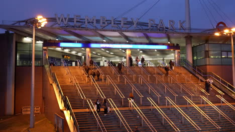 People-walk-up-and-down-the-steps-leading-to-the-main-entrance-of-Wembley-Park-Underground-train-station-at-dusk