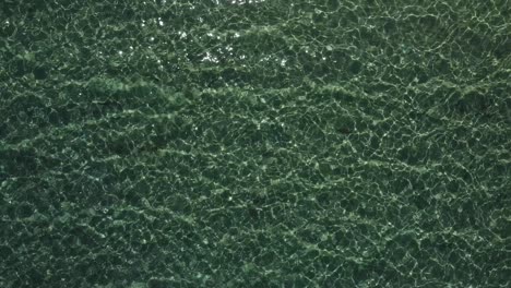 Top-down-aerial-view-of-a-shallow-bay-water-glistening-in-the-sun