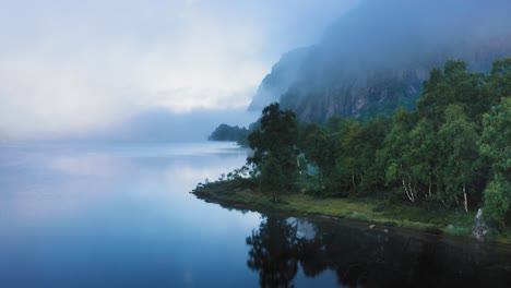 Thin-morning-fog-hangs-above-the-still-mirrorlike-waters-of-the-lake-and-engulfs-forest-covered-mountains