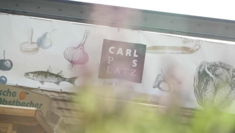 High-resolution-video-of-the-entrance-of-Carlsplatz-in-Düsseldorf,-a-prominent-white-banner-hangs-above-the-entrance,-featuring-painted-images-of-a-fish,-garlic,-salt,-and-a-pear
