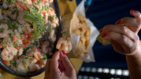 Vertical-slow-motion-of-a-female-hand-squeezing-a-lime-on-a-tortilla-chip-with-shrimp-from-a-traditional-mexican-ceviche-with-avocado