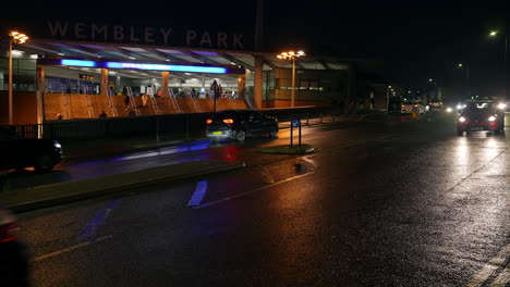 Cars-pass-by-on-the-wet-road-in-front-of-Wembley-Park-Underground-train-station-at-night