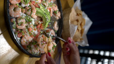 Vertical-slow-motion-of-a-woman-preparing-eating-a-tortilla-chip-with-shrimp-ceviche-prepared-with-onion-and-tomato
