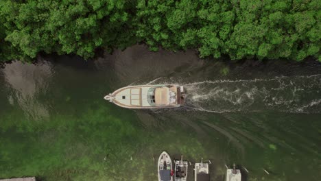 Drop-down-aerial-view-boat-navigating-canal-water-in-Riviera-Maya,-Mexico
