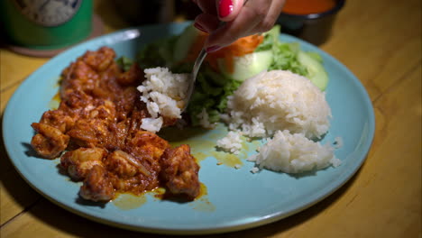 Slow-motion-close-up-a-woman-eating-a-traditional-mexican-shrimp-dish-with-white-rice-and-salad-using-a-spoon