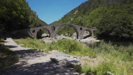 Approaching-shot-of-the-picturesque-landscape-of-Arda-River-and-the-historical-Devil's-Bridge-right-next-to-the-Rhodope-Mountains,-in-Ardino,-Bulgaria