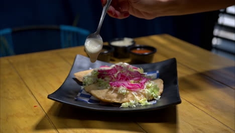 Slow-motion-of-a-woman-pouring-sour-cream-on-a-plate-of-traditional-mexican-empanadas-served-with-lettuce-and-red-onion