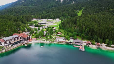 Aerial-view-of-the-beautiful-emerald-water-of-Eibsee-lake-in-Bavaria,-Germany,-with-a-lakeside-resort-at-the-base-of-the-Zugspitze-mountain,-surrounded-by-forest-of-pine-trees