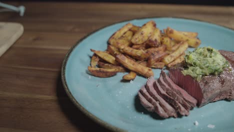 Beef-cut-with-fries,-accompanied-by-cafe-paris-butter,-served-on-a-blue-plate