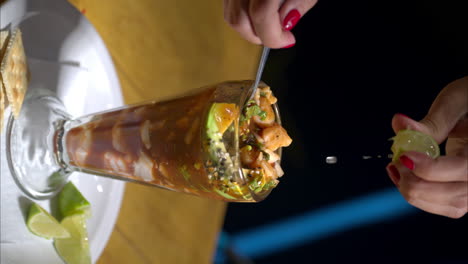 Vertical-slow-motion-shot-of-a-woman-hands-squeezing-a-lime-into-a-seafood-cocktail-served-in-an-old-fashion-glass-at-a-traditional-restaurant-in-Mexico