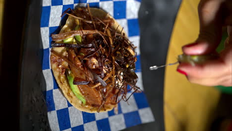 Vertical-slow-motion-of-a-seafood-tostada-with-fried-onion-strips-placed-on-a-blue-checkered-paper-and-a-woman-squeezing-a-lime-on-top