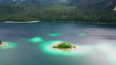 Aerial-view-of-little-islands-in-a-luminescent-lake,-surrounded-by-wilderness-of-pine-trees-at-the-base-of-Zugspitze-mountain