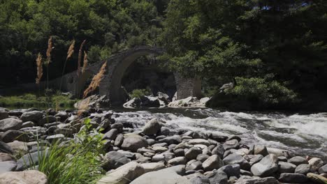 Gushing-waters-of-the-Arda-River-flowing-right-under-the-historical-Devil's-Bridge,-situated-in-a-forested-area-of-Rhodope-Mountains,-in-Ardino,-Bulgaria
