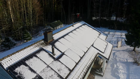 Aerial-view-rising-around-a-melting-roof-with-photovoltaic-cells,-winter-day