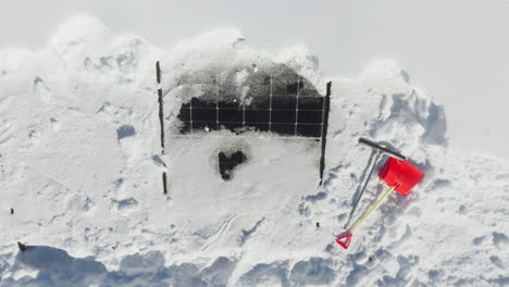 Aerial-view-of-a-plastic-shovel-and-a-rubber-scraper-at-snowy-solar-cells-on-a-house-roof
