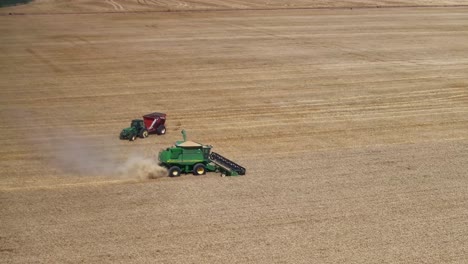 Aerial-view-of-harvester-working-and-tractor-and-bin-coming-alongside-for-harvester-unloading